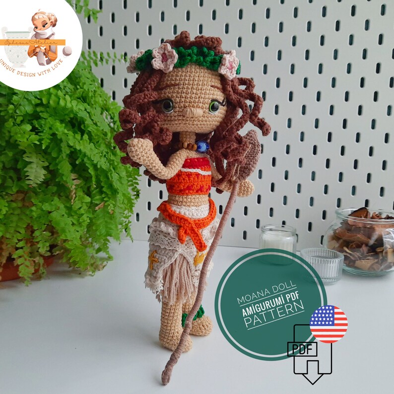 May include: A handmade crochet doll depicting a character with brown curly hair, wearing a floral crown, and a two-piece outfit in orange, white, and beige. The doll holds a wooden staff. The image includes text that reads "Moana Doll Amigurumi PDF Pattern."