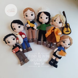 Könnte beinhalten: Sechs gehäkelte Amigurumi-Puppen, inspiriert von den Charakteren der Fernsehserie "Friends". Die Puppen sind in Outfits gekleidet, die an die charakteristischen Looks der Figuren erinnern. Die Puppen stehen alle auf einer weißen Oberfläche. Der Text "FRIENDS: ALL IN ONE AMIGURUMI DOLL PATTERN SET" ist unter den Puppen gedruckt.