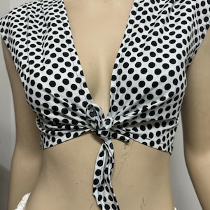 May include: A white crop top with black polka dots and a tie front. The top has short sleeves and a deep V-neck.
