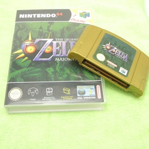 May include: A gold-colored Nintendo 64 game cartridge and game box for "The Legend of Zelda: Majora's Mask." The box features a green background with the game's title and a mask graphic. The cartridge is labeled with the game's title.