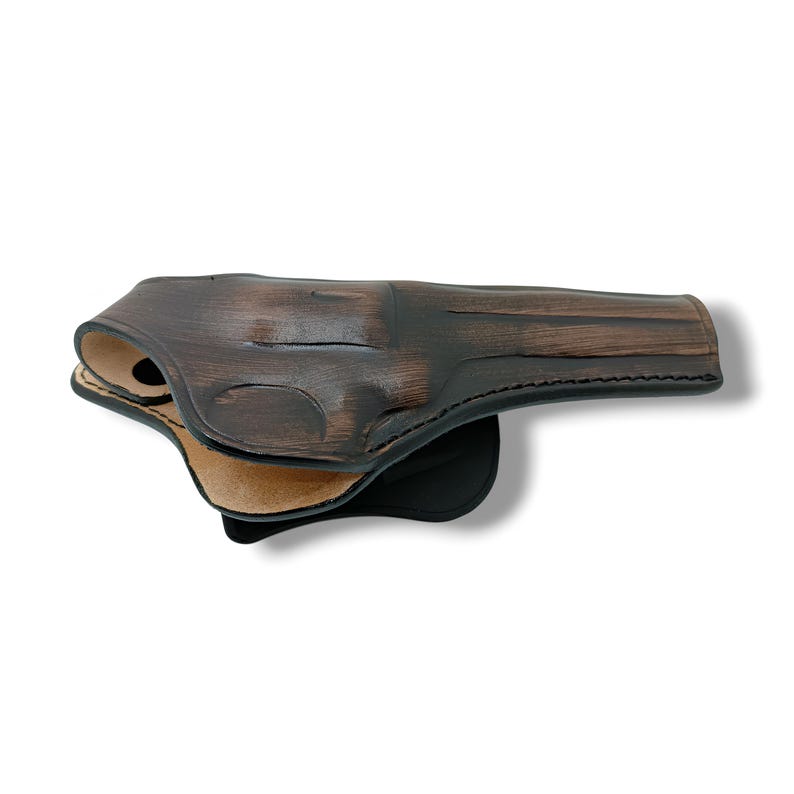 Puede incluir: Una funda de cuero marr&oacute;n con un acabado oscuro y envejecido. La funda est&aacute; dise&ntilde;ada para guardar una pistola y presenta un borde cosido y un interior de color claro. El dise&ntilde;o general es robusto y funcional.