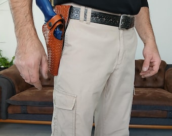 May include: A person wearing beige cargo trousers with a brown leather holster and a blue handgun. The person is wearing a black shirt and a black belt with a decorative buckle.