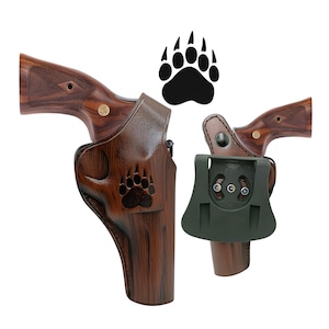Puede incluir: Dos fundas de pistola de cuero marr&oacute;n con un dise&ntilde;o de huella de pata de oso. Una funda est&aacute; sujeta a un rev&oacute;lver con un mango de vetas de madera. La otra funda est&aacute; sujeta a un rev&oacute;lver con un accesorio verde oscuro. Una huella de pata de oso negra est&aacute; encima de las fundas.