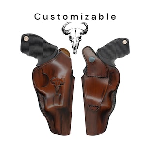 Könnte beinhalten: Zwei braune Lederholster mit einem Schädel-Design. Die Holster sind für einen Revolver und haben einen schwarzen Griff. Der Text "Customizable" befindet sich oben im Bild.