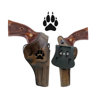 Puede incluir: Se muestran dos rev&oacute;lveres con empu&ntilde;aduras de madera, cada uno en una funda diferente. Una funda es de cuero marr&oacute;n con un dise&ntilde;o de huella de pata, y la otra es de pol&iacute;mero negro. Un gr&aacute;fico de huella de pata negra est&aacute; encima de las fundas.