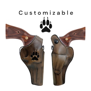 May include: Two brown leather gun holsters with a paw print design, displayed with the text "Customizable" above. The holsters are shown with the wooden handles of the guns. The holsters are made of brown leather.