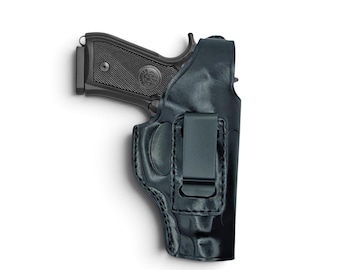 Op de afbeelding: Een zwarte lederen holster met een zwart semi-automatisch pistool. De holster is voorzien van een stevige metalen riemclip die met zichtbare stiksels aan de voorzijde is bevestigd. De pistoolgreep heeft een textuur en een rond logo-embleem.