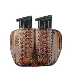 Może przedstawiać: Brązowy skórzany uchwyt na magazynki z wzorem plecionki, mieszczący dwa czarne magazynki. Uchwyt ma konstrukcję na dwa magazynki i jest wykonany z teksturowanej skóry.