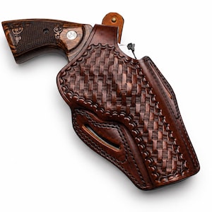 May include: A dark brown leather holster featuring a basket-weave pattern and stitched edges, containing a revolver with a dark wood grip that has intricate scrollwork engravings and a metallic emblem embedded on the side of the handle.