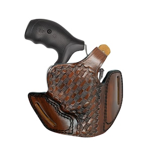 Könnte beinhalten: Ein braunes Lederholster mit einem gewebten Korbgeflechtmuster, das einen schwarzen Revolver hält. Das Holster hat einen dunkelbraunen Rand und eine hellbraune Innenseite. Der Griff des Revolvers ist schwarz und strukturiert.