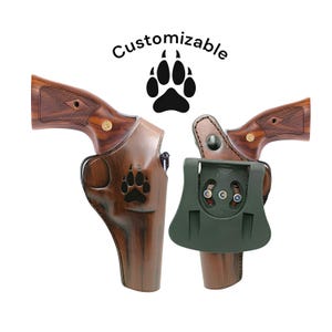 Puede incluir: Dos fundas de pistola de cuero marr&oacute;n con un dise&ntilde;o de huella de pata y un clip de cintur&oacute;n verde. El texto "Customizable" y un gr&aacute;fico de huella de pata est&aacute;n encima de las fundas.