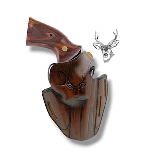 Può includere: Una fondina in pelle marrone con un design a testa di cervo, che tiene una rivoltella con impugnatura in legno. La fondina ha una finitura scura e strutturata e bordi cuciti. Un'illustrazione della testa di un cervo è accanto.