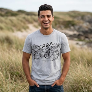 May include: A heather grey short-sleeved t-shirt featuring a black ink-style graphic of a mountain biker on a trail. The text reads TRAIL at the top and MOUNTAIN BIKE CO EST. 1994 at the bottom of the illustration, positioned centrally on the chest.