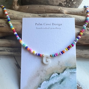 May include: A colourful beaded necklace with a white letter G charm. The necklace is on a card that says "Palm Cove Design handcrafted jewellery".