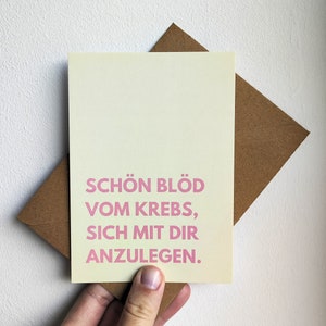May include: A light yellow card with a pink message that reads "Schon blod vom Krebs, sich mit dir anzulegen."