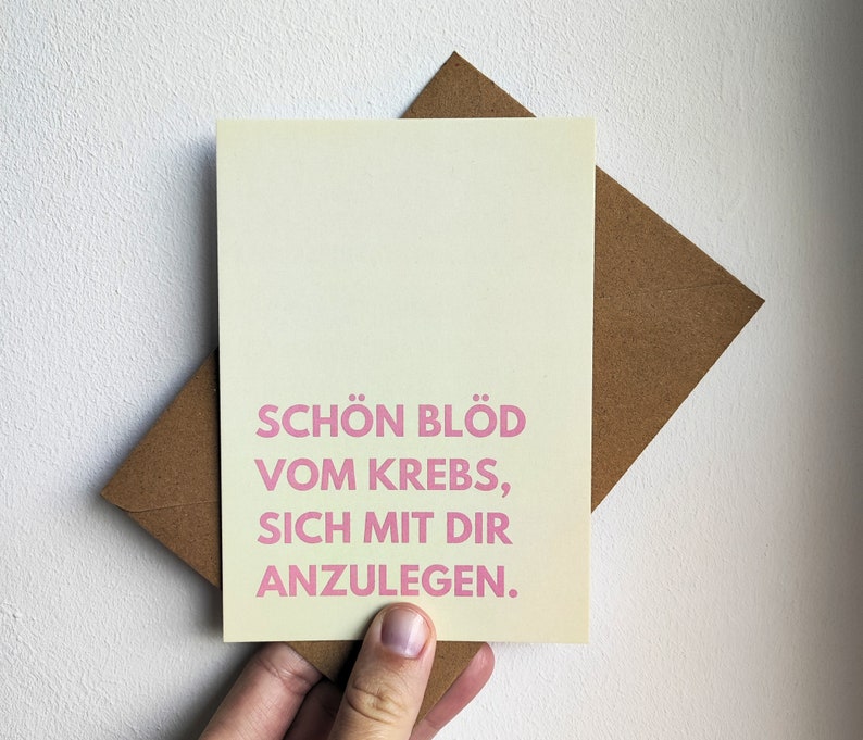 May include: A light yellow card with a pink message that reads "Schon blod vom Krebs, sich mit dir anzulegen."