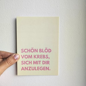 May include: A light yellow card with pink text that reads "Sch&ouml;n bl&ouml;d vom Krebs, sich mit dir anzulegen."