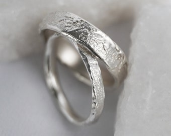 May include: Two silver rings with a textured finish, stacked on top of each other. The rings are on a white background.