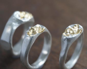 May include: Three silver rings with gold accents. The rings are all different shapes and sizes, but they all have a similar design. The gold accents are in the shape of small, irregular pieces of metal.