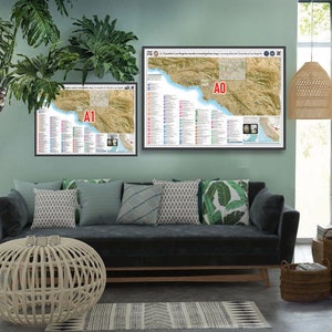 May include: Two framed maps of a coastal region with detailed information and a legend. The maps are hanging on a light green wall above a dark gray sofa with pillows. The sofa is in a living room with a potted plant, a wicker ottoman, and a woven pendant light.