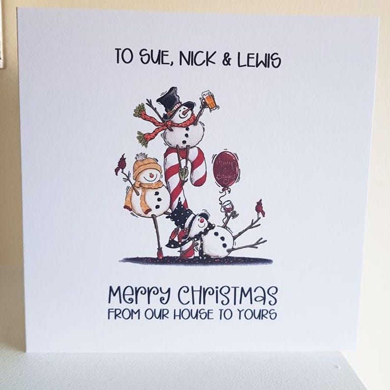 May include: A white Christmas card with a whimsical illustration of snowmen. The top text reads "TO SUE, NICK & LEWIS." The bottom text says "MERRY CHRISTMAS FROM OUR HOUSE TO YOURS." The snowmen are wearing hats and scarves.