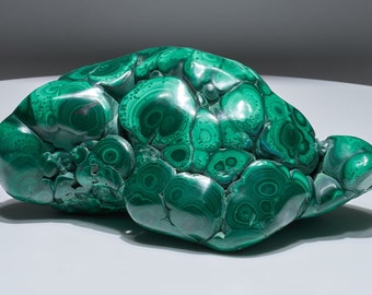 May include: A large, green malachite stone with a swirling, concentric pattern. The stone has a smooth, polished surface and is irregularly shaped.