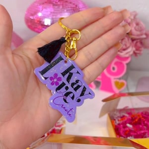 May include: Purple keychain with a black tassel and the text "I Kay. I Create." in black lettering. The keychain has a gold chain and a gold clasp.