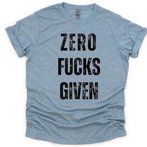 Puede incluir: Camiseta azul claro con el texto "ZERO FUCKS GIVEN" en fuente negra grande y desgastada. La camiseta tiene mangas enrolladas y cuello redondo. La tela parece suave y cómoda.