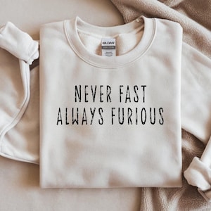 Peut inclure: Sweat-shirt crème avec l'inscription noire « NEVER FAST ALWAYS FURIOUS ». Les manches longues sont retroussées. Le vêtement est en matière douce, idéal pour un look décontracté.
