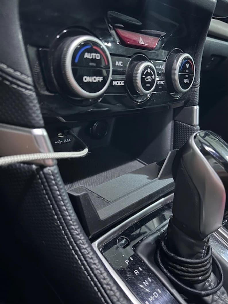 May include: Close-up of a car's interior dashboard featuring climate control knobs, a USB port, and a gear shift. The dashboard is black with silver accents. The climate control knobs have blue and red indicators.