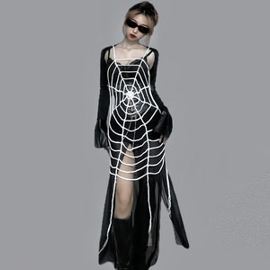 Puede incluir: Una mujer con un vestido negro con una superposición de telaraña blanca. Lleva botas negras y gafas de sol.