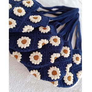 May include: A set of crocheted tote bags with daisy flower designs. The bags are navy blue with white and brown daisy flowers.