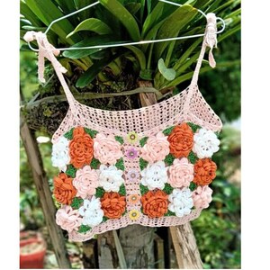 May include: A pink crocheted crop top with a floral design. The top features orange, white, and pink flowers.