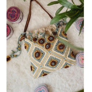 May include: A crocheted sunflower tote bag with brown straps and a light brown lining. The bag is made with a light blue and yellow yarn and features a repeating sunflower pattern.