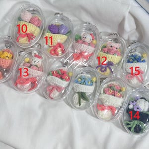 May include: A selection of clear, oval keyrings, each housing a miniature, handmade crochet design. The designs feature flowers, a bunny, and a teddy bear, in various colours. Each keyring is numbered for easy identification.