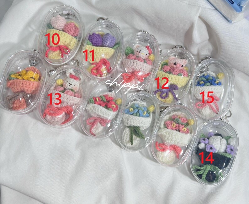 May include: A selection of clear, oval keyrings, each housing a miniature, handmade crochet design. The designs feature flowers, a bunny, and a teddy bear, in various colours. Each keyring is numbered for easy identification.