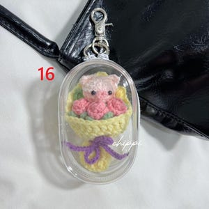 May include: A clear keychain featuring a crocheted bouquet and a pink pig. The bouquet has pink roses and yellow wrapping, tied with a purple bow. The number 16 is in red. The word "chippi" is visible.