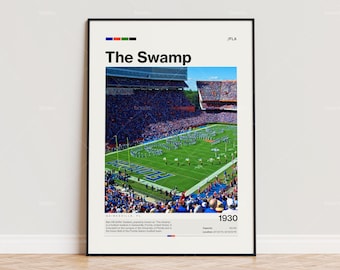 Op de afbeelding: Een ingelijste print met een luchtfoto van een vol voetbalstadion, met de tekst "The Swamp" en "1930". De print bevat de locatie en een korte beschrijving. De afbeelding toont een groen veld en blauwe zitplaatsen, met oranje en zwarte accenten.