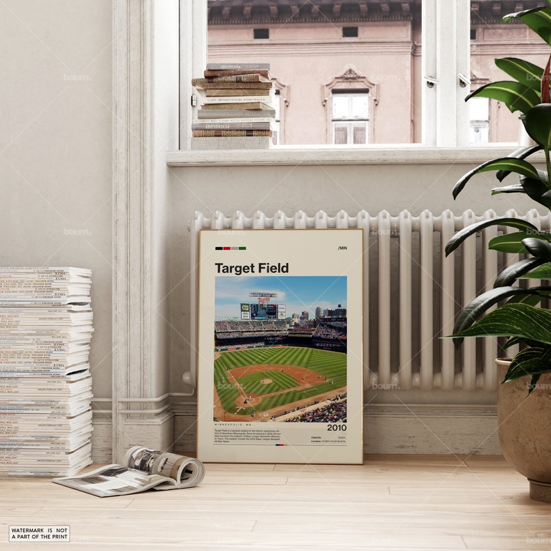 Op de afbeelding: Een ingelijste poster met Target Field honkbalstadion, met de tekst "Target Field" en "2010". De afbeelding toont het honkbalveld met groen gras, blauwe lucht en stadionzitplaatsen. De poster staat in een kamer met een raam en een radiator.