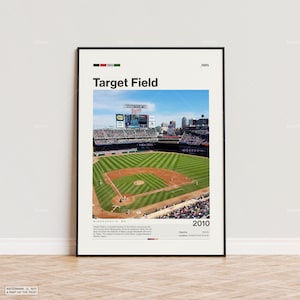 Op de afbeelding: Een ingelijste print van Target Field, een honkbalstadion in Minneapolis, MN. De afbeelding toont het veld, de tribunes en het scorebord onder een blauwe lucht. De tekst "Target Field" staat bovenaan, met "2010" onderaan. De print heeft een zwarte lijst.