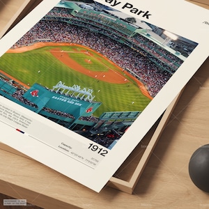 May include: A framed print of Fenway Park, home of the Boston Red Sox, with a bird's-eye view of the baseball field and stands filled with spectators. The print includes the text "Fenway Park Boston Red Sox", "Capacity 1912", and location coordinates.