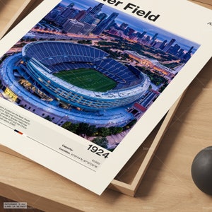 May include: A framed print featuring an aerial view of Soldier Field stadium in Chicago, Illinois. The stadium is lit up at dusk, with a green field and blue seating. The print includes the text "Soldier Field", the year 1924, and the stadium's capacity.