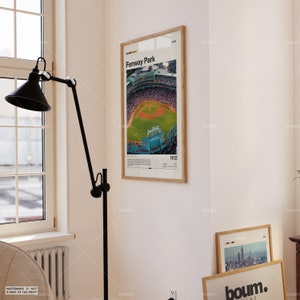 May include: A framed print of Fenway Park, a baseball stadium, with a bird's-eye view of the field. The print includes the text "Fenway Park" and the year "1912". The frame is light brown.