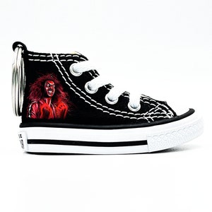May include: Black canvas Converse high-top shoe keychain with a red and black painted image of a person with red hair and a red jacket.