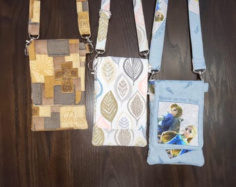 May include: Three crossbody cell phone pouches with adjustable straps. One is patchwork with religious text, another has a leaf pattern, and the third features a graphic from "Breath of the Wild". Each has a silver-tone clasp.