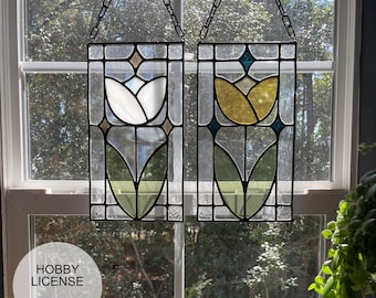 May include: Two stained glass panels featuring a tulip design. The panels are hung from chains and have a white and yellow tulip design with green leaves.