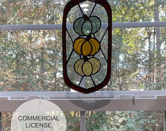 Puede incluir: Una ventana de vitral colgada de una cadena, con tres calabazas apiladas en tonos de verde, amarillo y naranja. Las calabazas están delineadas en negro y tienen un efecto de vidrio texturizado.