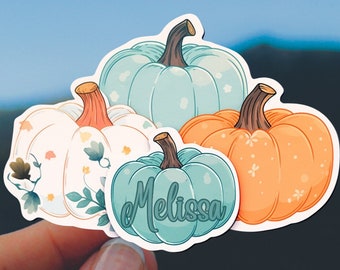 May include: A collection of pumpkin stickers in various colors, including orange, teal, and white, with green stems. One sticker has the name "Melissa" in teal script. The pumpkins are decorated with floral and leaf patterns.