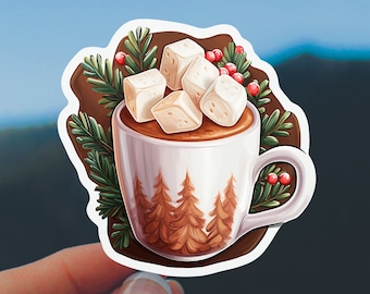 May include: A sticker featuring a white mug filled with hot chocolate and topped with marshmallows. The mug has a forest scene design. Green pine needles and red berries surround the mug, all set against a brown background. The sticker is held in a hand.