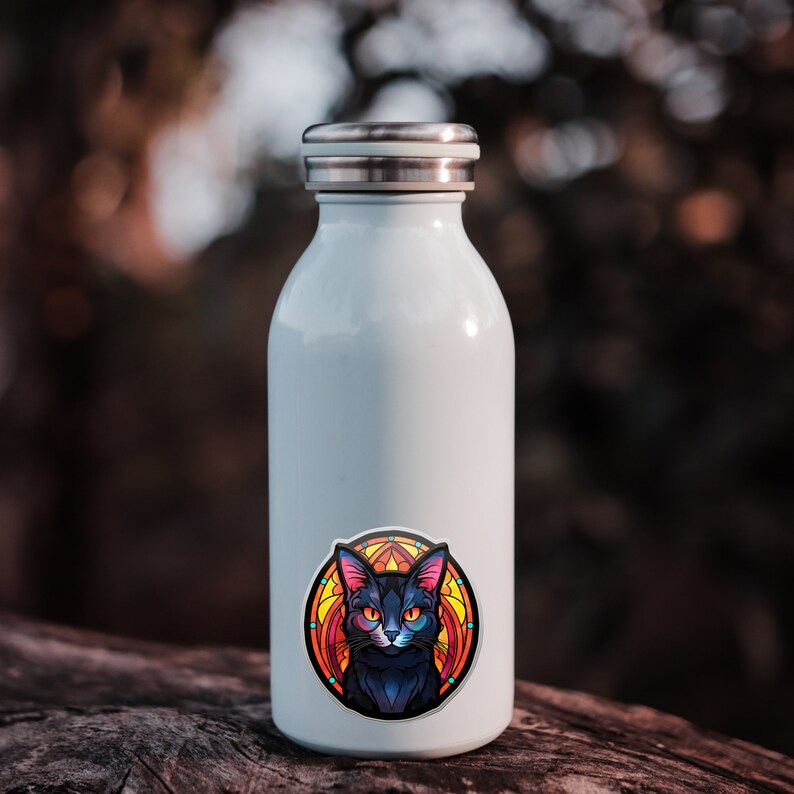 May include: A pale blue insulated water bottle with a silver lid. A circular sticker featuring a black cat with stained glass-style details is on the bottle. The cat has orange and blue eyes and pink ears.